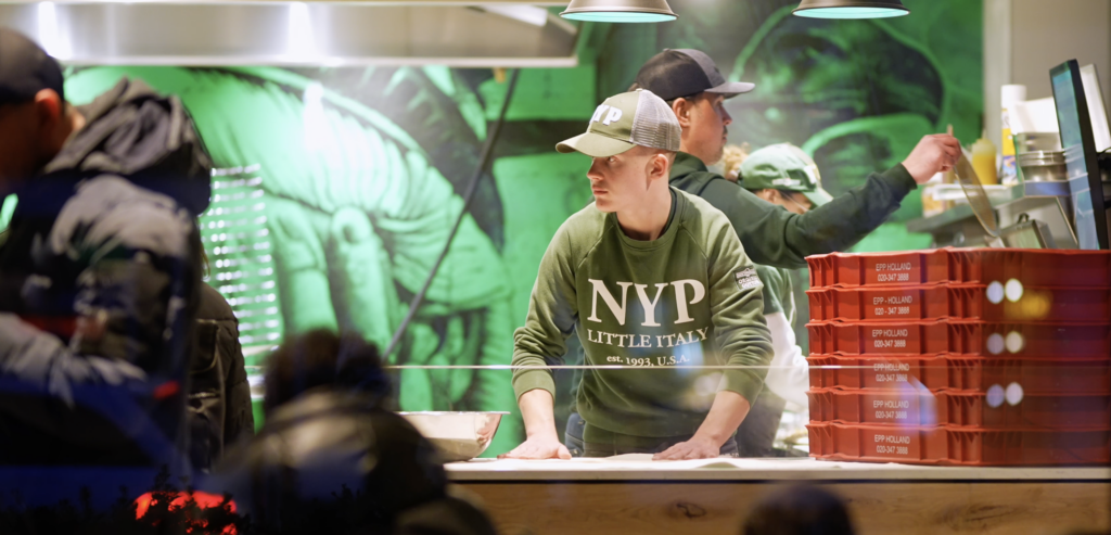 First Pizza Creation Image: Employee Crafting the Inaugural Pizza at New York Pizza's Grand Opening.