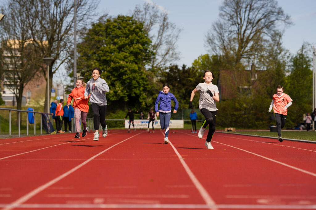 Een actievolle reportagefoto van kinderen die een sprint trekken op de atletiekbaan tijdens de Koningsspelen in Beverwijk, vastgelegd door Monutes.