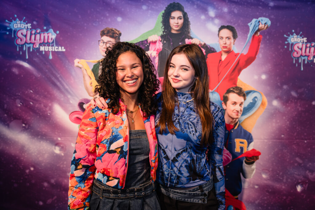 Actrice Zafanya Kersten en influencer/artiest Bibi poserend voor de perswand tijdens de première van De Grote Slijmmusical, gefotografeerd door Monutes.