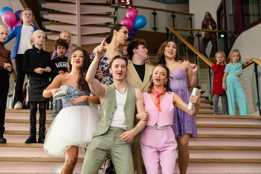 De cast van De Grote Slijmmusical zingend en poserend op de trap tijdens de feestelijke première, vastgelegd door Monutes.