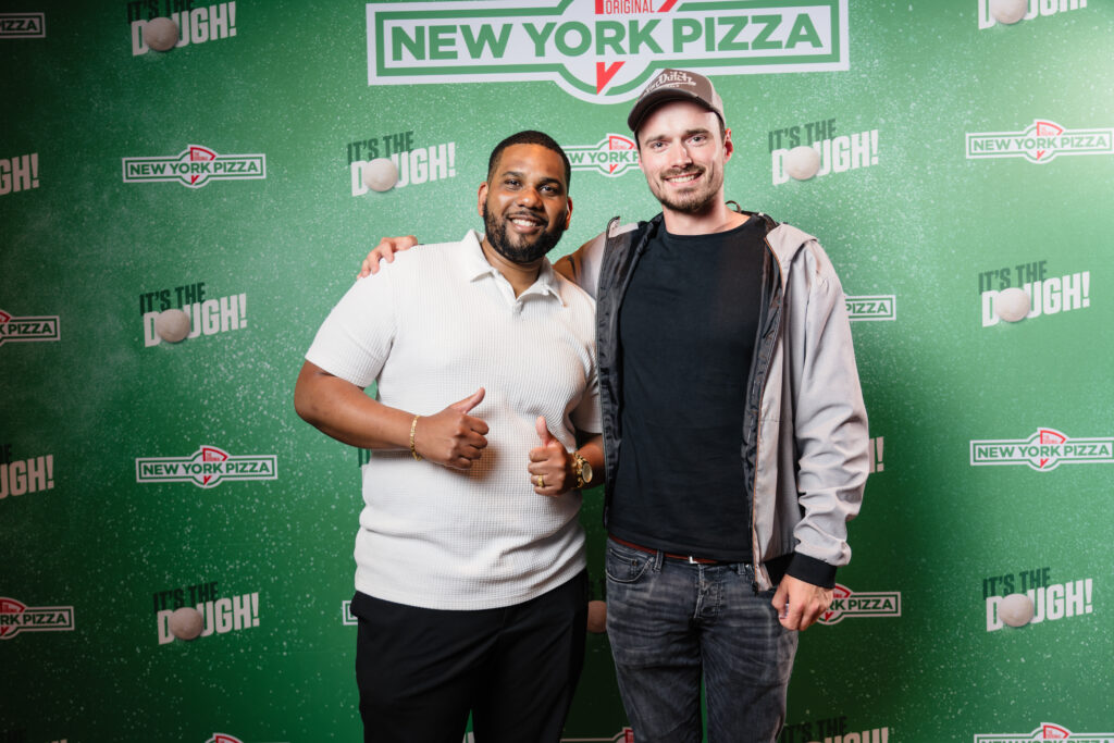 Twee franchisenemers van New York Pizza poseren lachend voor de perswand tijdens een bijeenkomst in het Bimhuis Amsterdam, gefotografeerd door Monutes.