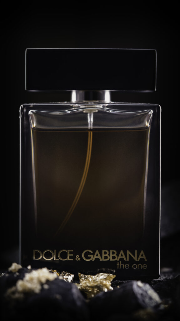 Een high-end productfoto van een Dolce & Gabbana The One parfumfles op een donkere ondergrond met goudsnippers en rotsachtige texturen, gefotografeerd door Monutes.