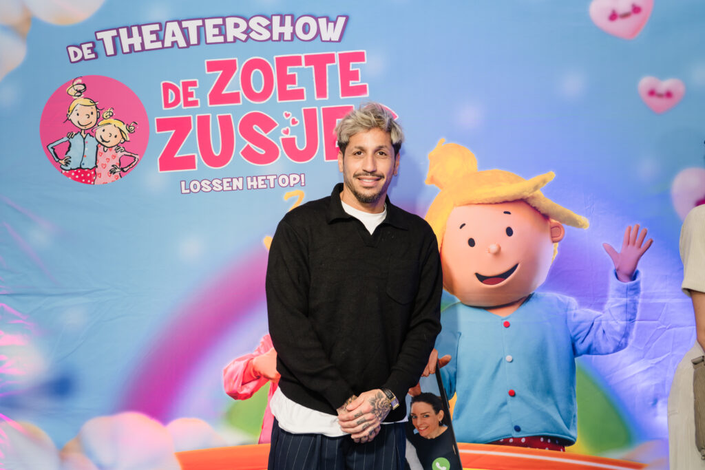 Artiest Jody Bernal poseert voor de perswand tijdens de première van de theatershow 'De Zoete Zusjes lossen het op', gefotografeerd door Monutes.
