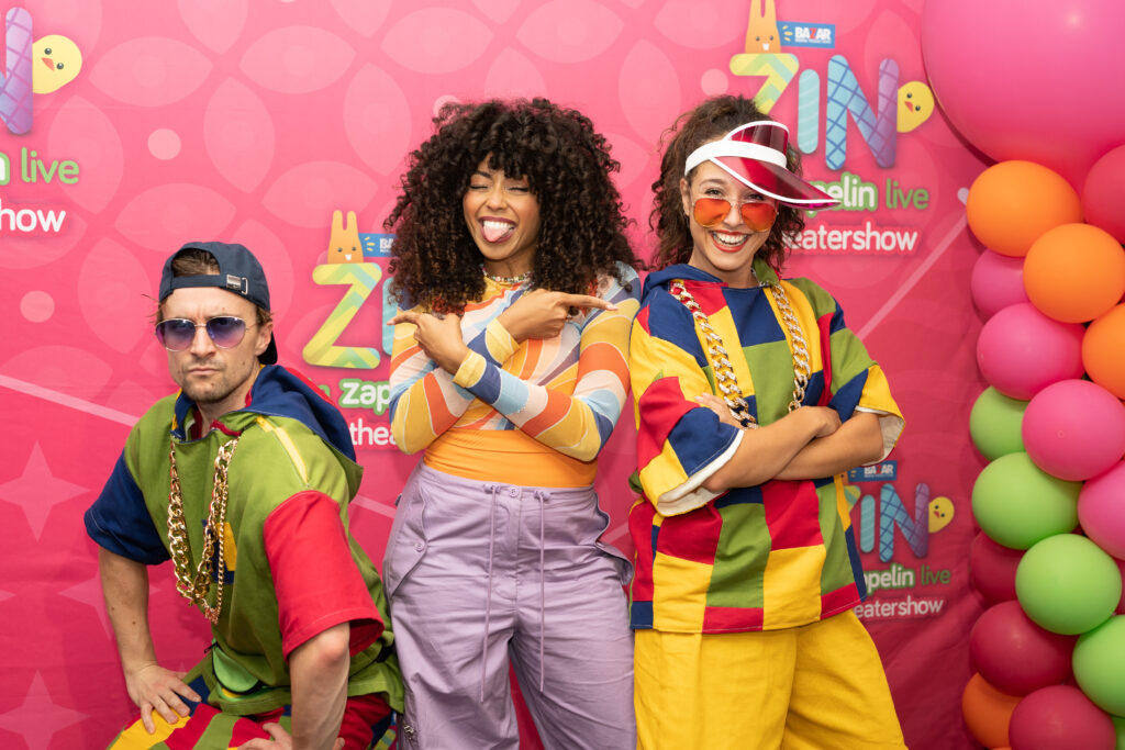 De cast van Zin in Zappelin Live, met onder andere Fenna Ramos, poserend voor de kleurrijke perswand tijdens de première van hun theatershow, gefotografeerd door Monutes.
