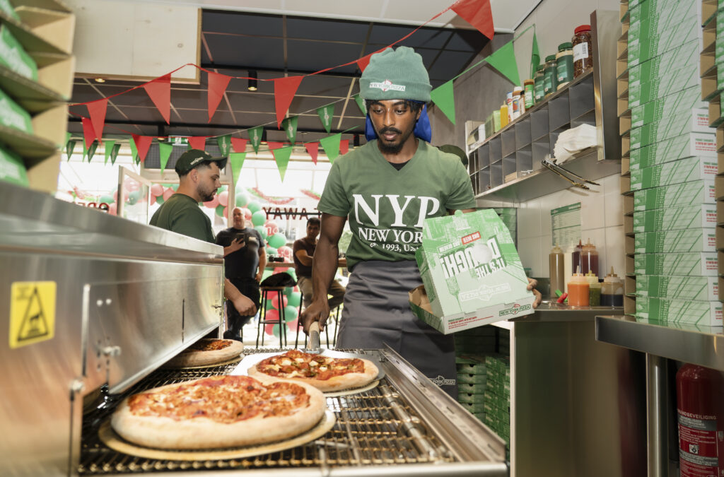 Een bedrijfsreportagefoto in een New York Pizza filiaal waarbij een medewerker verse pizza's uit de oven haalt, gefotografeerd door Monutes.