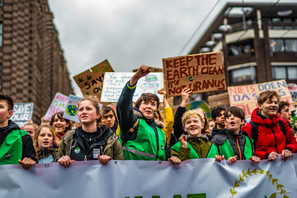 Een krachtige reportagefoto van protesterende jongeren tijdens een klimaatstaking, met spandoeken en borden voor een betere toekomst, gefotografeerd door Monutes.