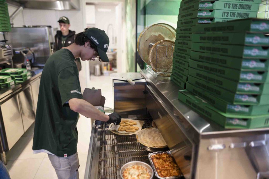 Medewerker bereidt pizza's in de keuken van de nieuwe New York Pizza vestiging in Nieuwkoop