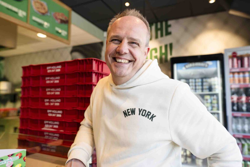 Lachende franchisehouder in wit New York-hoodie bij de opening van zijn New York Pizza vestiging in Nieuwkoop